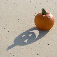 Pumpkin on the sand with face cut out of the shadow.